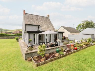 A two-story house with a patio area featuring outdoor furniture and plants at Pondfield Gate in Cwmgors