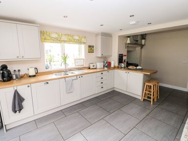 A kitchen with white cabinets wooden countertops a window with a yellow floral blind and two wooden stools at Pondfield Gate in Cwmgors