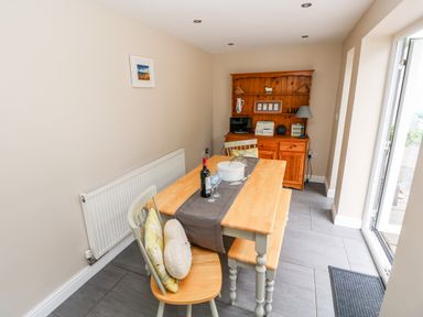 A dining area with a wooden table, chairs with cushions, a sideboard, and an open door at Pondfield Gate in Cwmgors