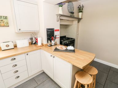 A kitchen corner with white cabinets wooden countertop two wooden stools and a stove at Pondfield Gate in Cwmgors