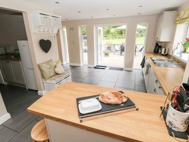 A kitchen with wooden countertops a loaf of bread on a cutting board and a seating area near the door to the patio at Pondfield Gate in Cwmgors