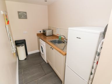 A laundry room with a washing machine a sink a microwave a refrigerator and a trash bin at Pondfield Gate in Cwmgors