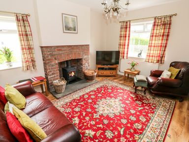 A living room with a red patterned rug a brick fireplace two leather armchairs and plaid curtains at Pondfield Gate in Cwmgors