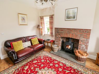 A living room with a leather sofa, wood-burning stove in a brick fireplace, and a red floral rug at Pondfield Gate in Cwmgors