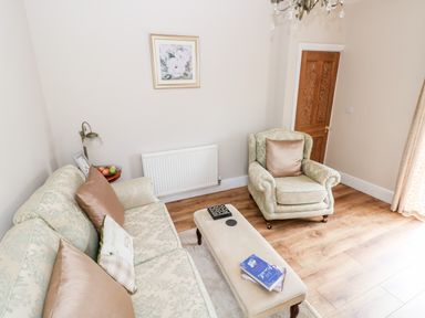 A sitting room with patterned sofa armchair a bench with books hardwood flooring and a door at Pondfield Gate in Cwmgors