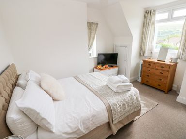 A bedroom with a bed a chest of drawers a tv on a cabinet and windows with curtains at Pondfield Gate in Cwmgors