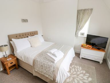 A bedroom with a bed, bedside table with lamp, TV on cabinet, window with curtain at Pondfield Gate in Cwmgors