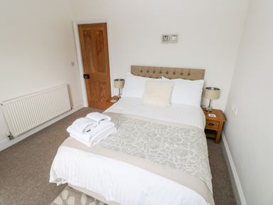 A bedroom with a double bed white linens bedside tables lamps and folded towels on the bed at Pondfield Gate in Cwmgors
