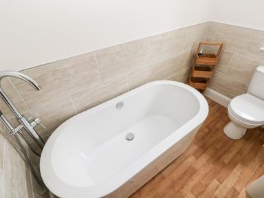 A bathroom with a white freestanding bathtub a chrome tap wooden floor toilet and a small wooden shelf at Pondfield Gate in Cwmgors