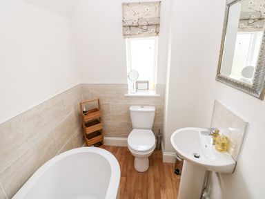 A bathroom with a bathtub toilet wooden shelf sink and window at Pondfield Gate in Cwmgors