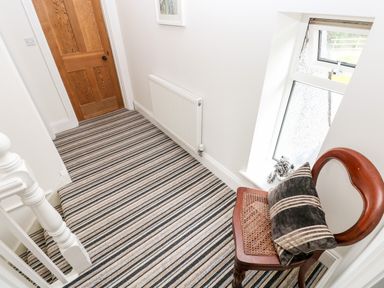 A hallway with striped carpet wooden door white walls a wooden chair with a pillow and a small window at Pondfield Gate in Cwmgors