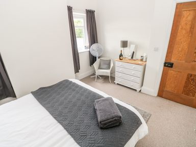 A bedroom with a bed with folded towels a white dresser chair and window with curtains at Pondfield Gate in Cwmgors