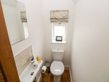 A small bathroom with a toilet sink mirror and a window with a floral blind at Pondfield Gate in Cwmgors