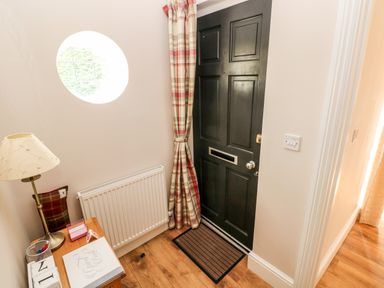 An entryway with a dark door and striped curtain next to a small wooden table with a lamp and papers at Pondfield Gate in Cwmgors