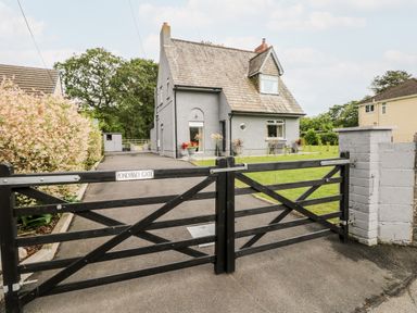 A grey house with a tiled roof behind a closed black wooden gate with a driveway and grass at Pondfield Gate in Cwmgors