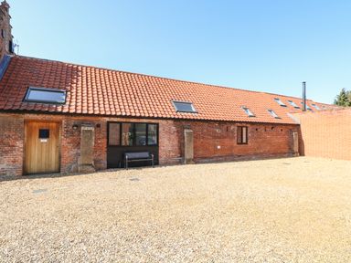 A red brick building with a tiled roof and skylights with a wooden door and a bench outside at The Long Barn in Morton on the Hill near Lenwade