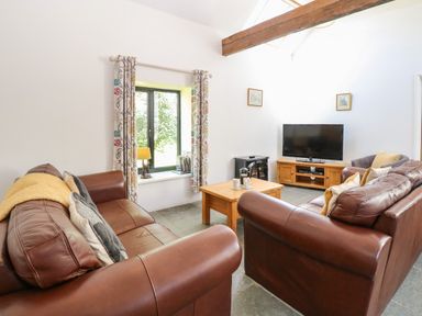 A living room with brown leather sofas a wooden coffee table a television on a stand and a window with floral curtains at The Long Barn in Morton on the Hill near Lenwade
