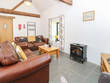 A living room with brown leather sofas a wooden coffee table a window with curtains and a black stove at The Long Barn in Morton on the Hill near Lenwade