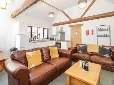 An open living room and kitchen with brown leather sofas and wooden beams at The Long Barn in Morton on the Hill near Lenwade