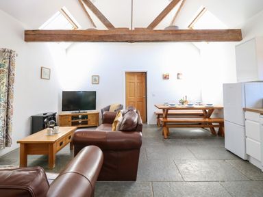 A living room with brown leather sofas a wooden coffee table a TV wooden dining table with benches and a fridge at The Long Barn in Morton on the Hill near Lenwade