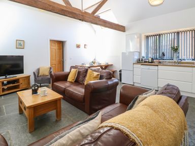 A living room with brown leather sofas a wooden coffee table a TV and an open kitchen with white cabinets at The Long Barn in Morton on the Hill near Lenwade