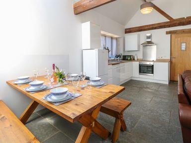 A kitchen with wooden dining table set with dishes and glasses next to white cabinets and appliances at The Long Barn in Morton on the Hill near Lenwade
