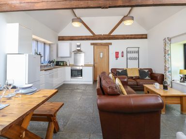An open plan room with a kitchen and seating area with brown leather sofas and a wooden dining table at The Long Barn in Morton on the Hill near Lenwade