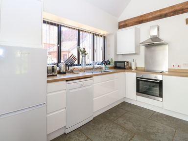A kitchen with white cabinets wooden countertops and a window with vertical blinds at The Long Barn in Morton on the Hill near Lenwade