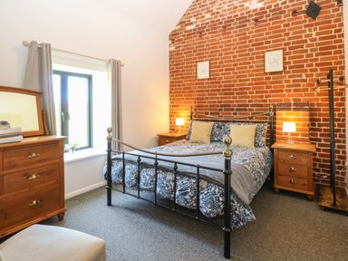 A bedroom with a metal bed frame a blue floral bedspread two bedside tables with lamps a wooden dresser and a window at The Long Barn in Morton on the Hill near Lenwade