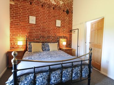 A bedroom with a metal bed frame against a brick wall and bedside tables with lamps at The Long Barn in Morton on the Hill near Lenwade