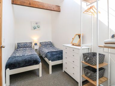 A bedroom with two single beds a white chest of drawers an open wardrobe with hangers and storage baskets at The Long Barn in Morton on the Hill near Lenwade