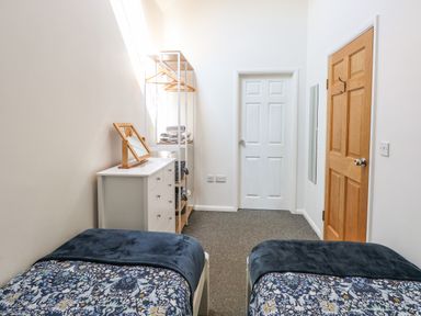 A bedroom with two single beds a white dresser a shelving unit with towels and hangers two doors and a mirror at The Long Barn in Morton on the Hill near Lenwade