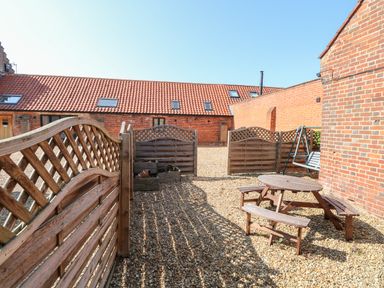 An outdoor gravel area with wooden fencing a picnic table and a swing seat at The Long Barn in Morton on the Hill near Lenwade