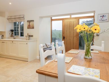 A kitchen and dining area with a wooden table and white chairs yellow flowers on the table and a wooden door at Lavender Cottage in Market Weighton