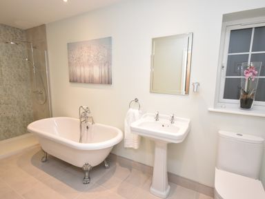 A bathroom with a clawfoot bathtub pedestal sink toilet and window with a vase of flowers at Lavender Cottage in Market Weighton