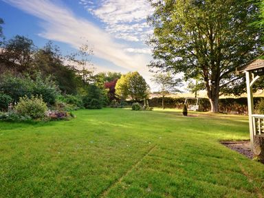 A garden with a lawn trees bushes a swing and a wooden gazebo at Lavender Cottage in Market Weighton