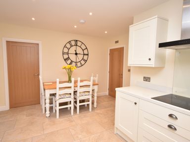 A kitchen with a wooden dining table and white chairs a large wall clock and two wooden doors at Lavender Cottage in Market Weighton