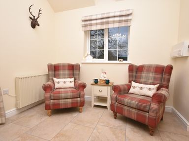 A seating area with two plaid armchairs and a small table between them under a window at Lavender Cottage in Market Weighton