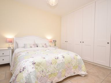 A bedroom with a bed and floral quilt next to nightstands with lamps and a wall of white wardrobes at Lavender Cottage in Market Weighton
