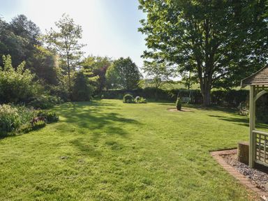 A garden with grass trees flowerbeds a swing and a gazebo at Lavender Cottage in Market Weighton