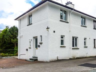 A white two storey house with multiple windows and a door with steps in front at Thompson Cottage in Ambleside