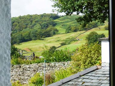 A view of green hills trees and stone walls seen from a window at Thompson Cottage in Ambleside