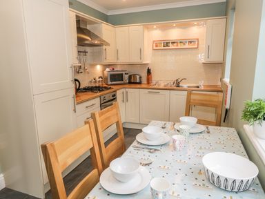 A kitchen with white cabinets wooden countertops a dining table set with bowls cups and cutlery at Thompson Cottage Ambleside