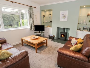 A living room with two leather sofas coffee table television and a wood-burning stove at Thompson Cottage in Ambleside