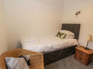 A bedroom with a single bed with white bedding and a butterfly pillow a wooden bedside table with a lamp and a wicker chair with a cushion at Thompson Cottage in Ambleside