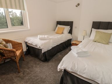 A bedroom with two single beds a wicker chair and a window at Thompson Cottage in Ambleside