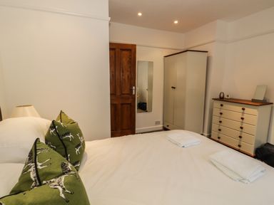 A bedroom with a bed with green pillows and white towels a wardrobe a chest of drawers and a wooden door at Thompson Cottage in Ambleside
