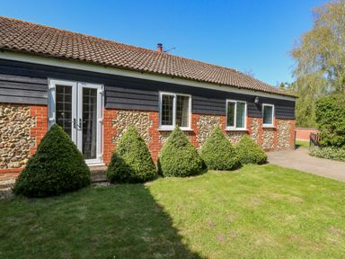 A house with a tile roof stone and brick walls and bushes in front at The Meadows Cottage in Billingford near Bawdeswell