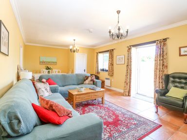 A living room with teal sofas a wooden coffee table a red patterned rug and a green armchair at The Meadows Cottage in Billingford near Bawdeswell