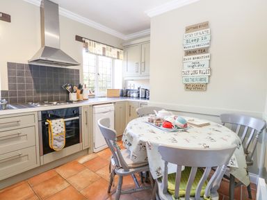 A kitchen with a round table and four chairs a stove with an oven and a hood near a window at The Meadows Cottage in Billingford near Bawdeswell